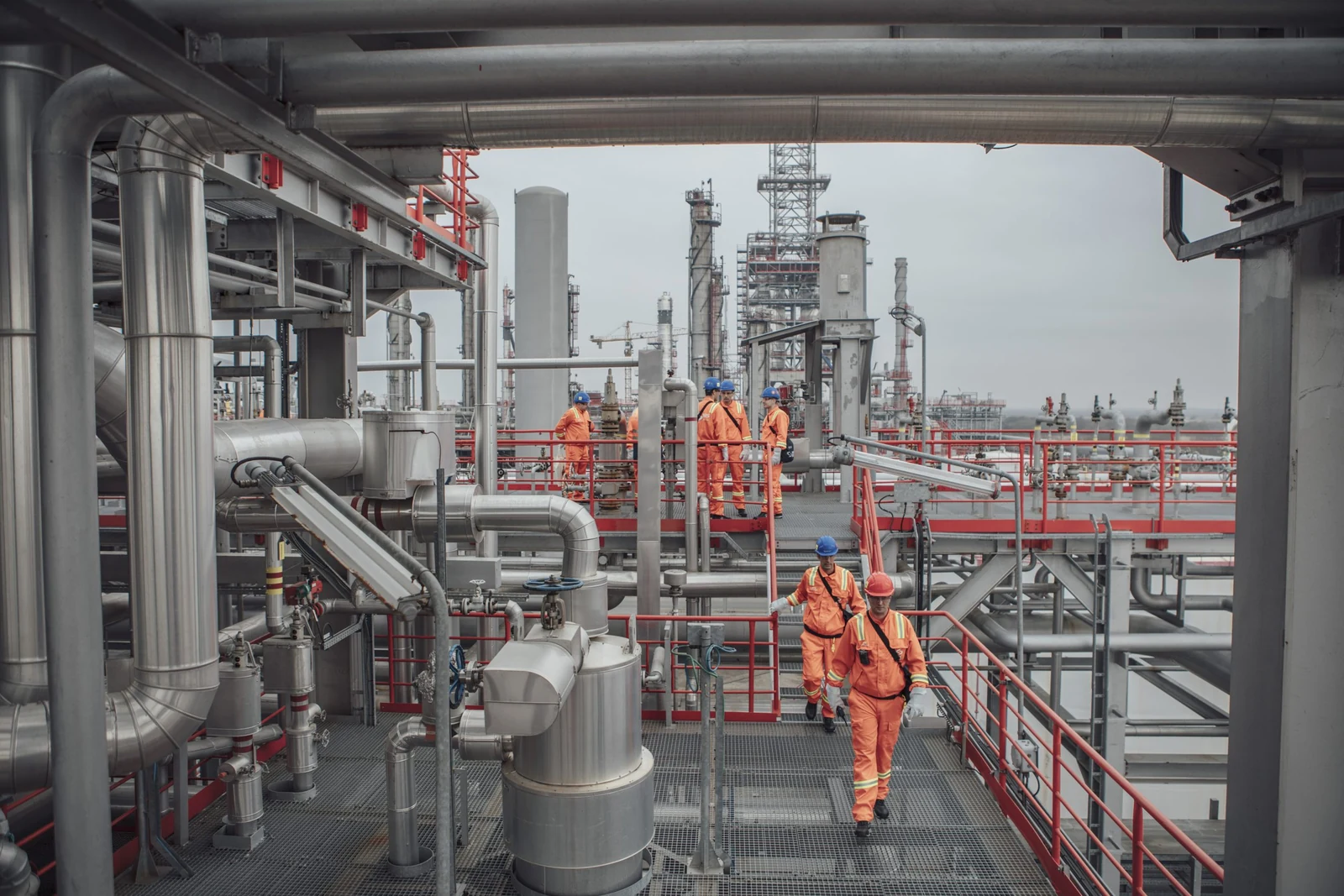 Refinery personnel in protective coveralls and hard hats on an industrial processing platform